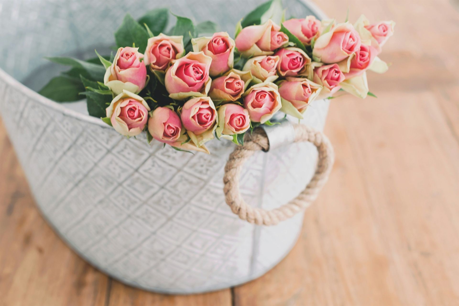 Bouquet of pink roses in a gray basket with rope handles on a wooden table.